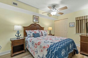 A bedroom with a bed, a ceiling fan, a nightstand, a lamp, and a door. - Bahama Sands Luxury PH3- 3 Bedrooms Oceanfront (North Myrtle Beach)