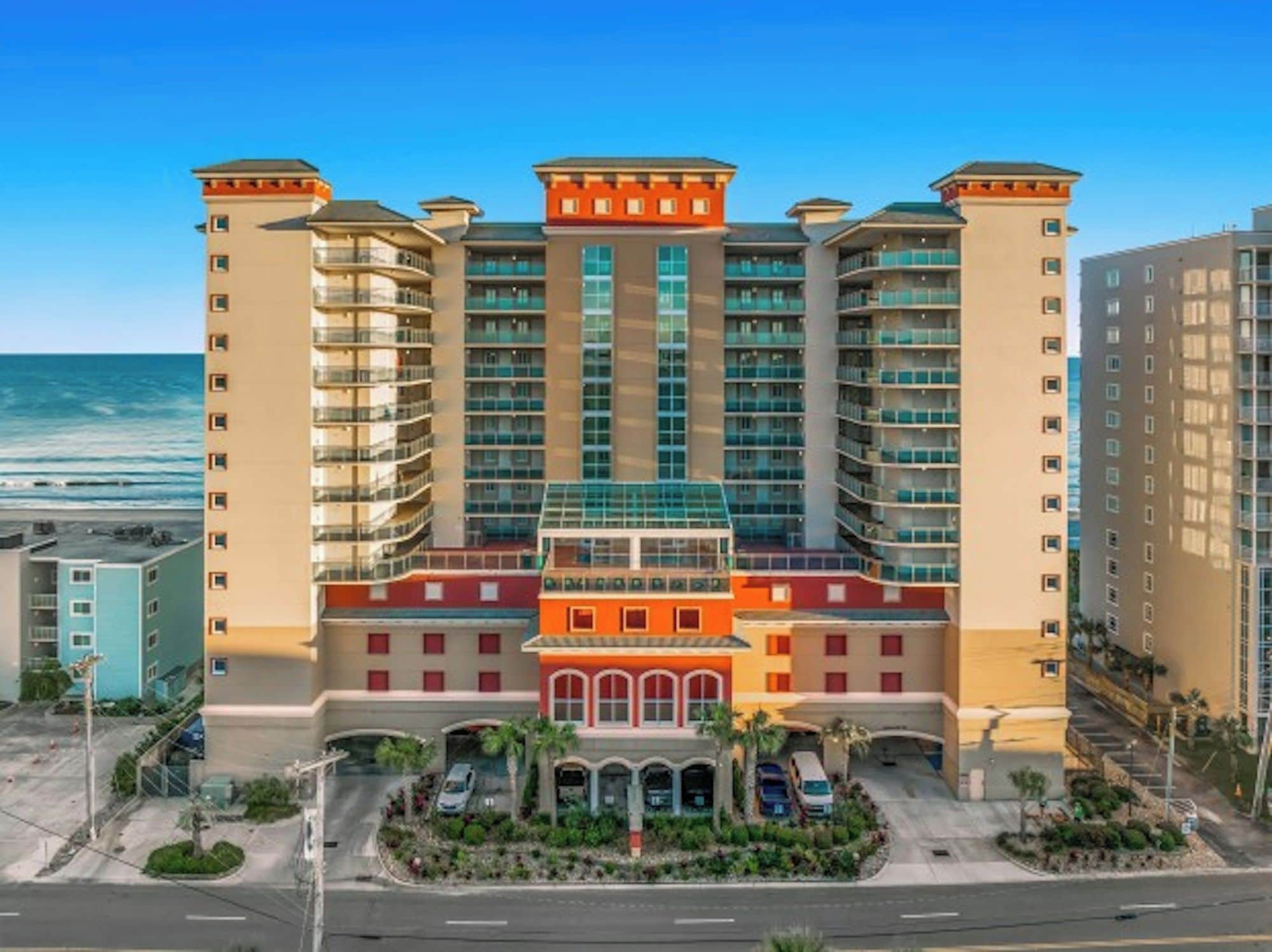 A multi-story hotel with a central courtyard, balconies, and a view of the ocean.