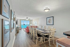 A spacious dining area with a long table, chairs, and a view of the ocean through large windows. - Bahama Sands Luxury PH3- 3 Bedrooms Oceanfront (North Myrtle Beach)