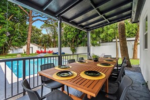 A covered outdoor dining area with a pool, surrounded by trees and a white fence. - Luxury 6BR 2-Home Retreat w/ Pool, BBQ & Games (Pompano Beach)