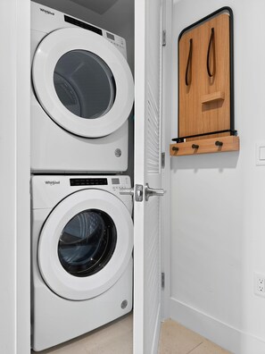 Un lavadero con dos lavadoras Whirlpool y un armario de madera con ganchos.