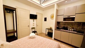Ein Hotelzimmer mit Bett, kleinem Tisch, Stuhl, Fernseher und einer Küchenzeile.