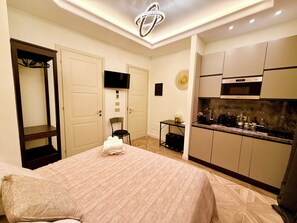 Una habitación de hotel con una cama, una mesita, una silla, un televisor y una kitchenette.