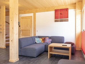 A modern interior with a grey sofa, colorful cushions, a wooden coffee table, and a red cabinet. - One-bedroom Cabin (Sankt Georgen am Kreischberg)
