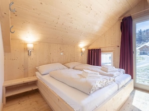 A wooden cabin bedroom with two beds, a window with curtains, and wall-mounted lights. - One-bedroom Cabin (Sankt Georgen am Kreischberg)