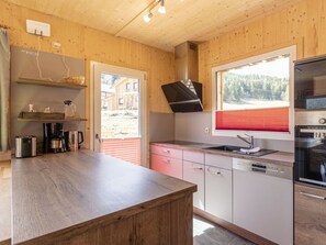 A modern kitchen with wooden cabinetry, a built-in oven, and a window with a view of a forested area. - One-bedroom Cabin (Sankt Georgen am Kreischberg)