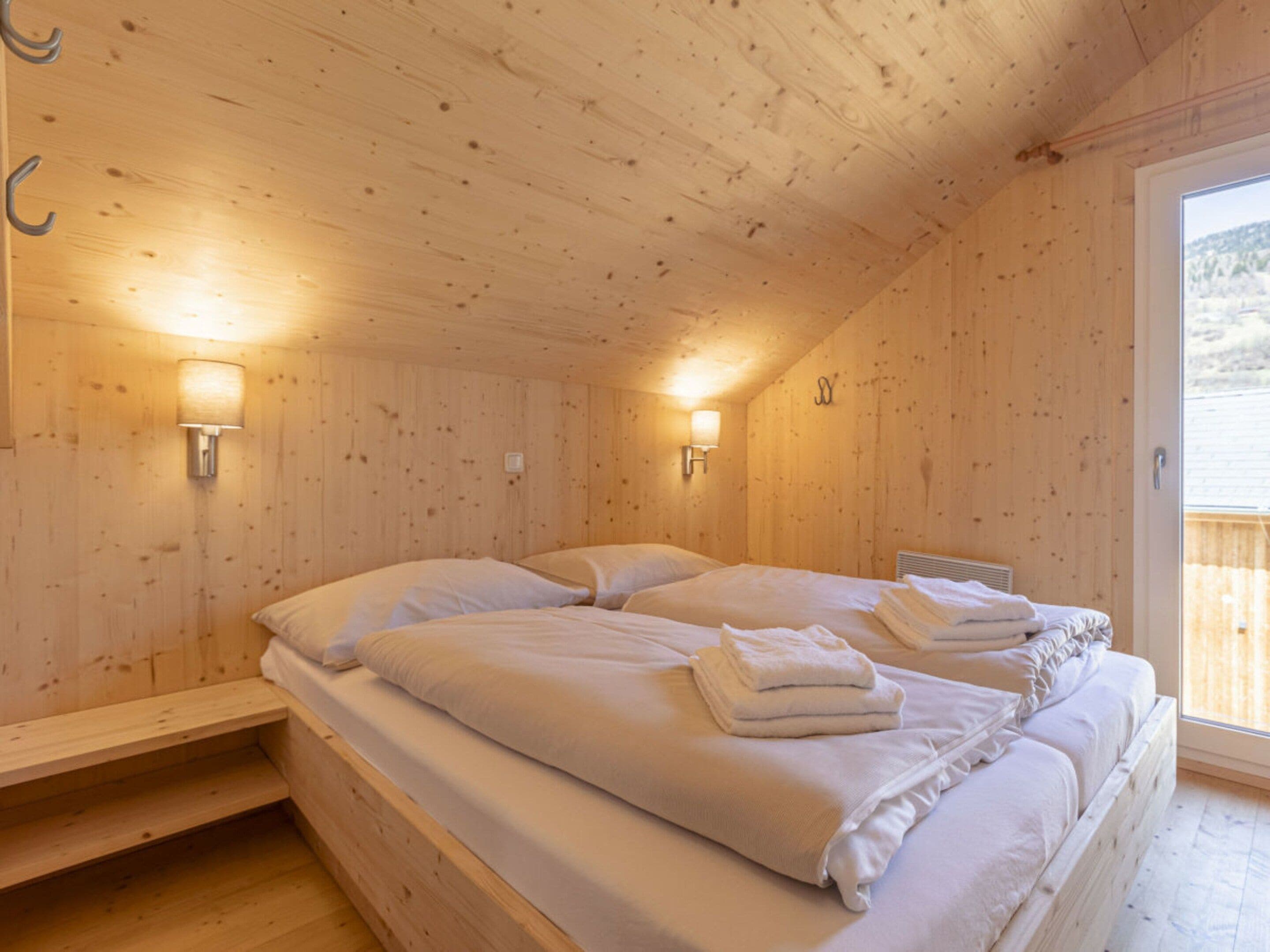 A wooden room with two beds, each with pillows and towels, and two wall-mounted lamps.