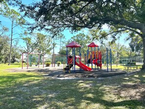 Ein Spielplatz mit roten und gelben Spielgeräten, darunter Rutschen und Schaukeln, umgeben von Bäumen und Gras.
