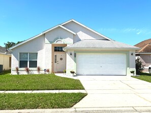 A single-story house with a garage, a front door, and a small front yard with grass and potted plants. - Family Oasis•15 min to Disney (Kissimmee)