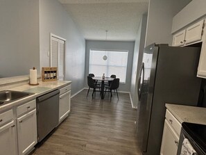A kitchen with a dishwasher, refrigerator, and a dining area with a table and chairs. - Family Oasis•15 min to Disney (Kissimmee)