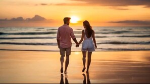 Un couple se promène sur une plage au coucher du soleil.