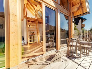 A wooden cabin with a glass door entrance, a patio with outdoor furniture, and a view of the surrounding landscape. - Chalet # Rfl006 for 2 People With Sauna (Oberwölz)