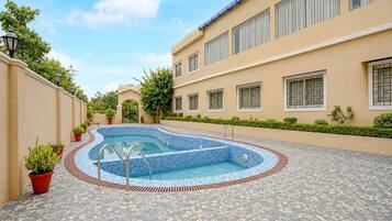 A swimming pool with a tiled deck, surrounded by a building with multiple windows and a gated entrance.