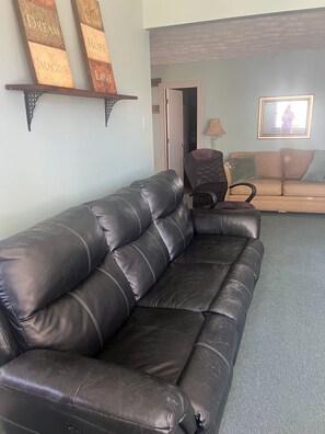 A black leather sofa in a living room with a door leading to another room, a lamp, and a framed picture on the wall.