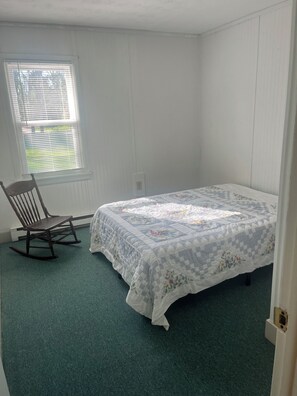 Un dormitorio con cama, mecedora y ventana con persianas.