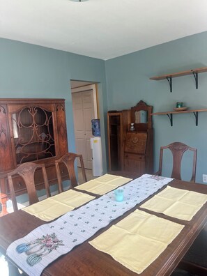 A dining room with a wooden table set for four, a water dispenser, and a door leading to another room.