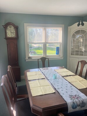 Ein Esszimmer mit gedecktem Tisch für vier Personen, einer Wanduhr und einem Fenster mit Jalousien.