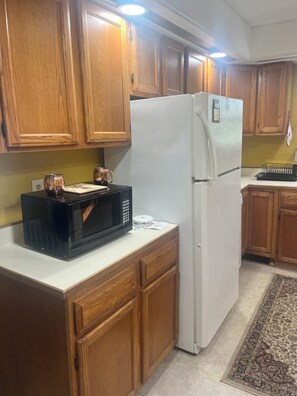 Una cocina con armarios de madera, un refrigerador blanco, un microondas negro y una cafetera sobre la encimera.