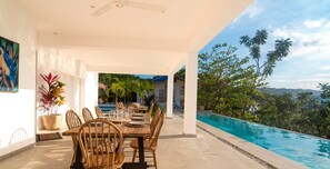 Ein Essbereich im Freien mit Blick auf einen Pool, Holzmöbel und einem Deckenventilator.