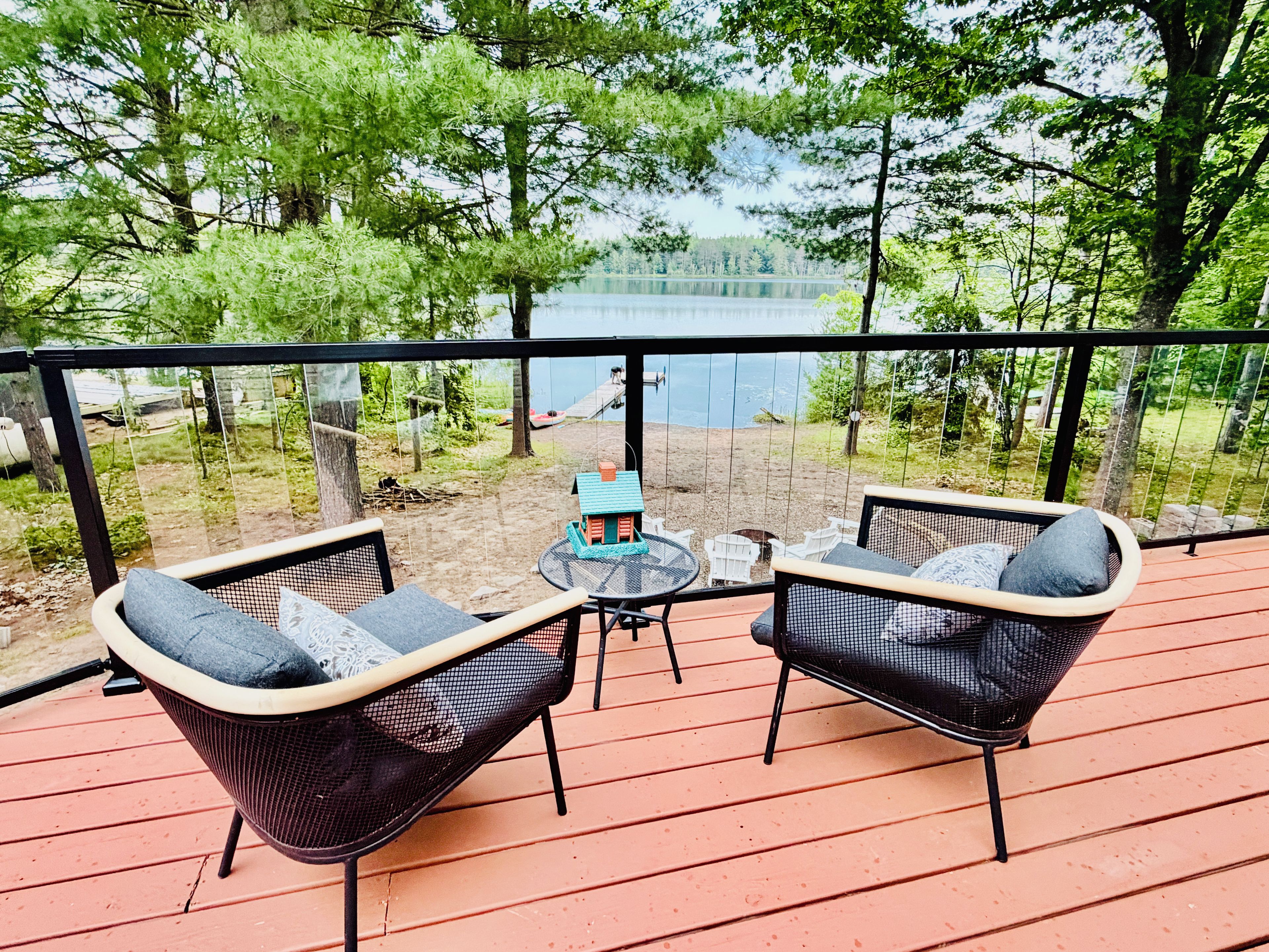 A deck with two wicker chairs and a small table, overlooking a lake and a sandy beach area.