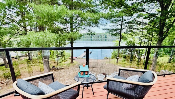 Eine Terrasse mit zwei Korbstühlen und einem kleinen Tisch, mit Blick auf einen See und einen Sandstrand.