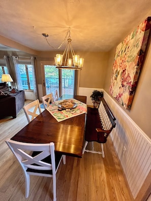 A dining area with a wooden table, white chairs, a chandelier, and a large floral painting on the wall. - Cozy 2-bedroom house in tranquil Frederic with AC (Frederic)