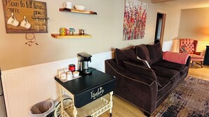 Ein gemütliches Wohnzimmer mit einem schwarzen Kaffee-Wagen, einem braunen Sofa, einer Wanddekoration und einem kleinen Regal mit Gegenständen.