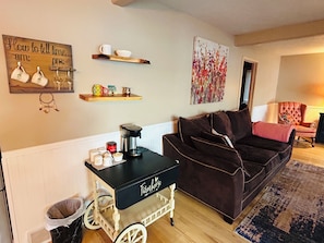 A cozy living room with a black coffee cart, a brown sofa, a decorative wall piece, and a small shelf with items. - Cozy 2-bedroom house in tranquil Frederic with AC (Frederic)
