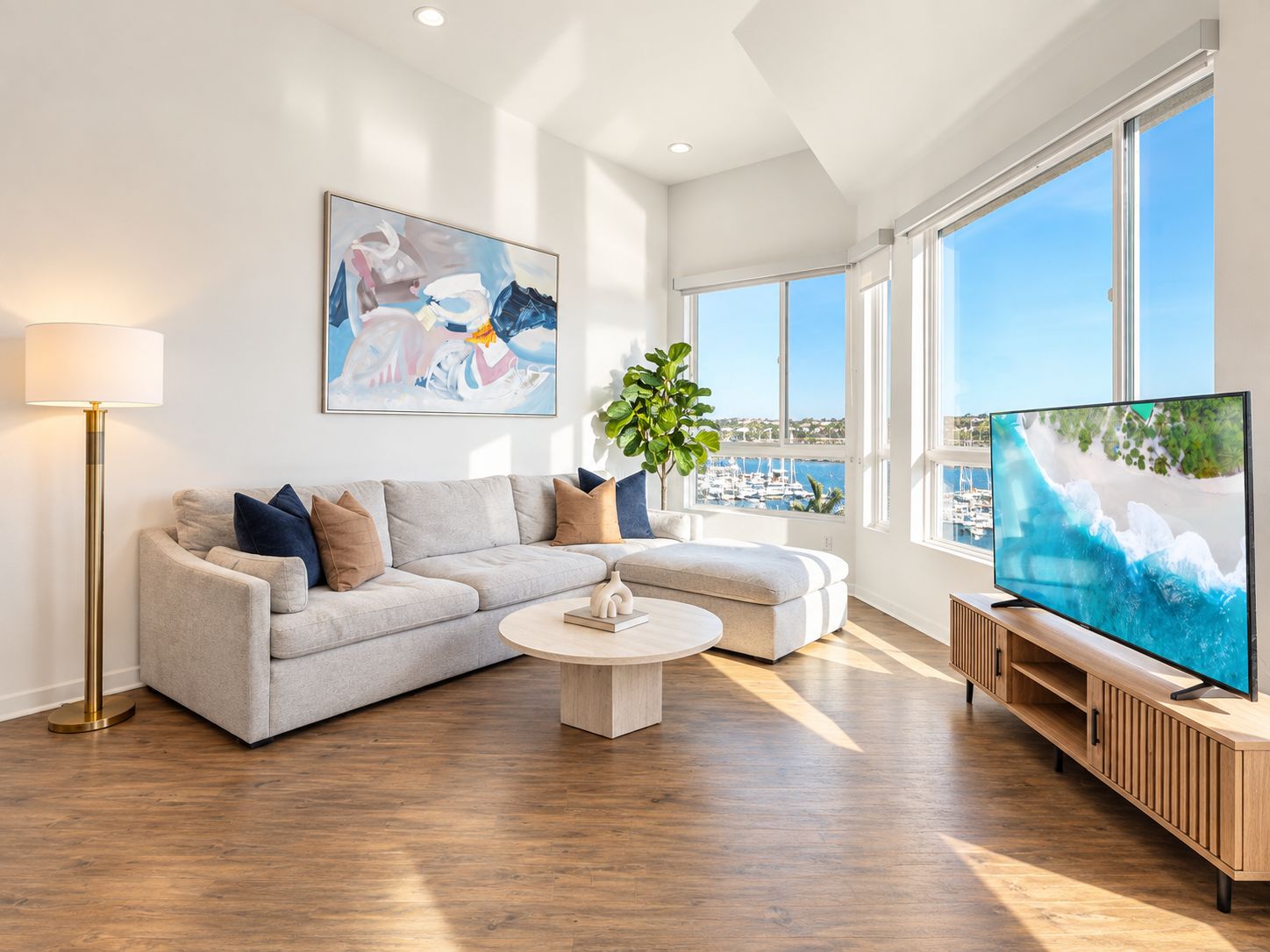 A modern living room with a sofa, coffee table, and TV, featuring a large window with a view of the sea.