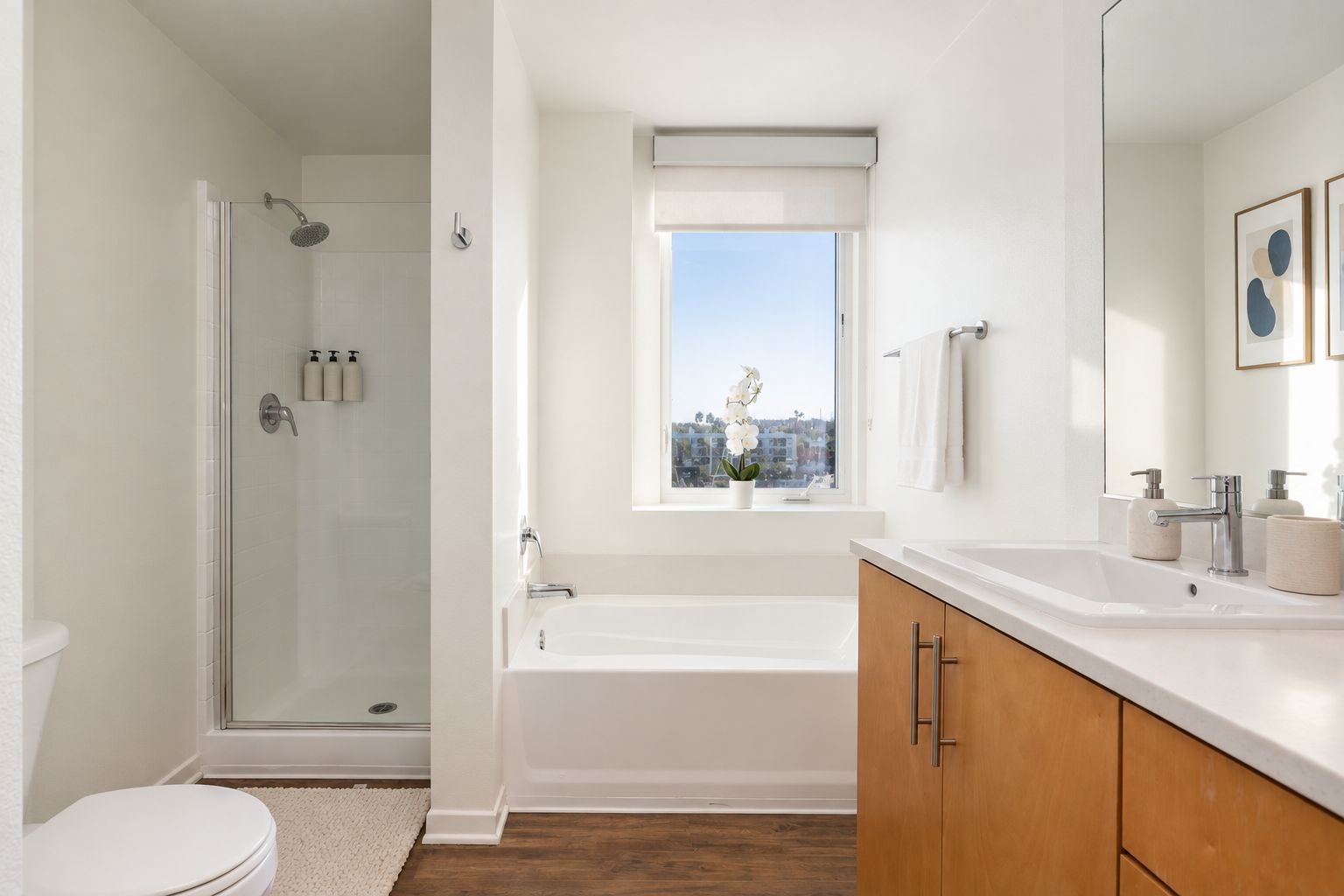 A modern bathroom with a glass-enclosed shower, a bathtub, a toilet, and a window with a city view.