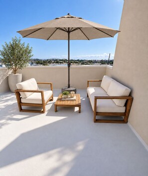 En takterrass med två trästolar, en beige soffa, ett träbord och ett stort parasoll.