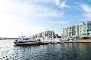 En småbåtshamn med flera yachter förtöjda, en modern byggnad med balkonger och en klar himmel.