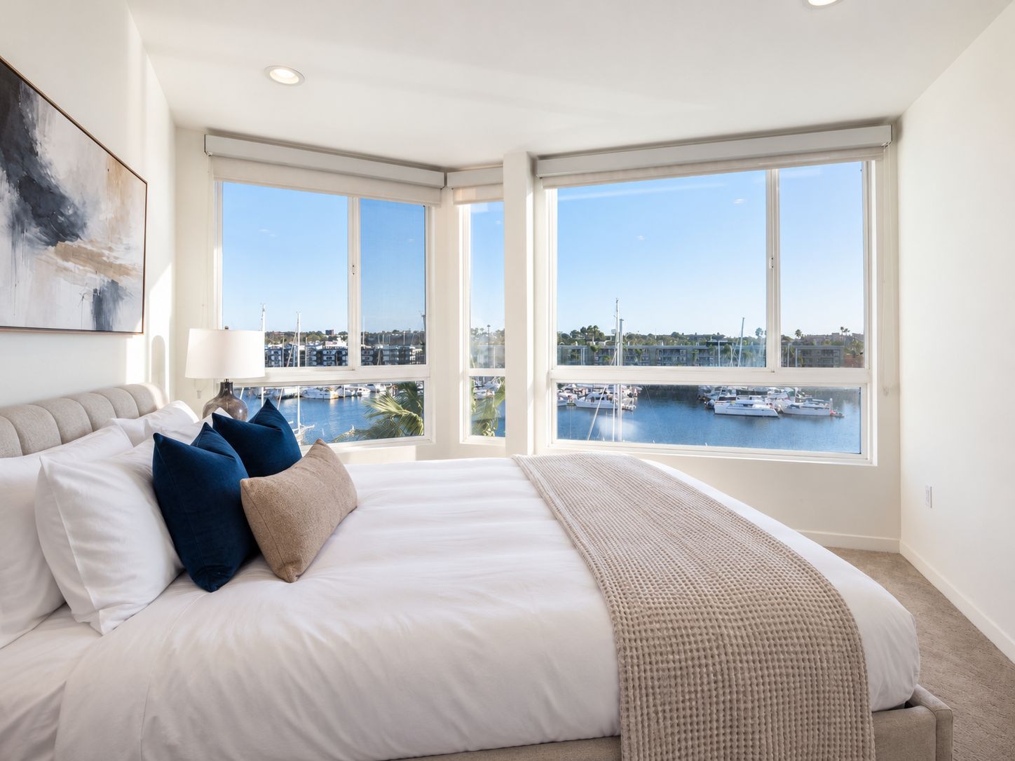 A bedroom with a large bed, a view of a marina, and a painting on the wall.