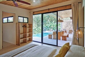 Ein Schlafzimmer mit einem großen Bett, einem Holzschrank, einer Hängeleuchte und Blick auf einen Außenpool.