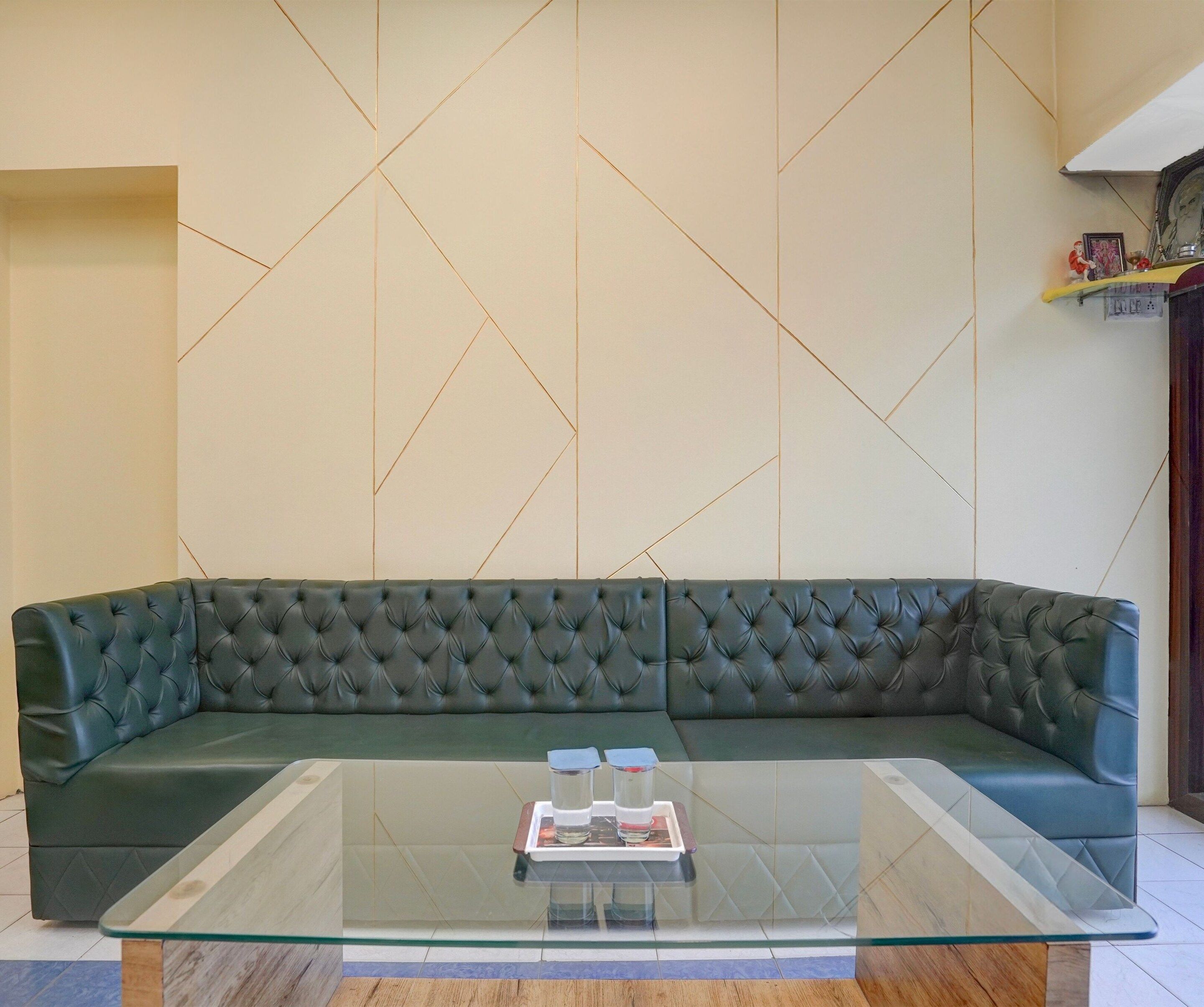 A modern living room with a dark green sectional sofa, a glass coffee table, and a geometric patterned wall.