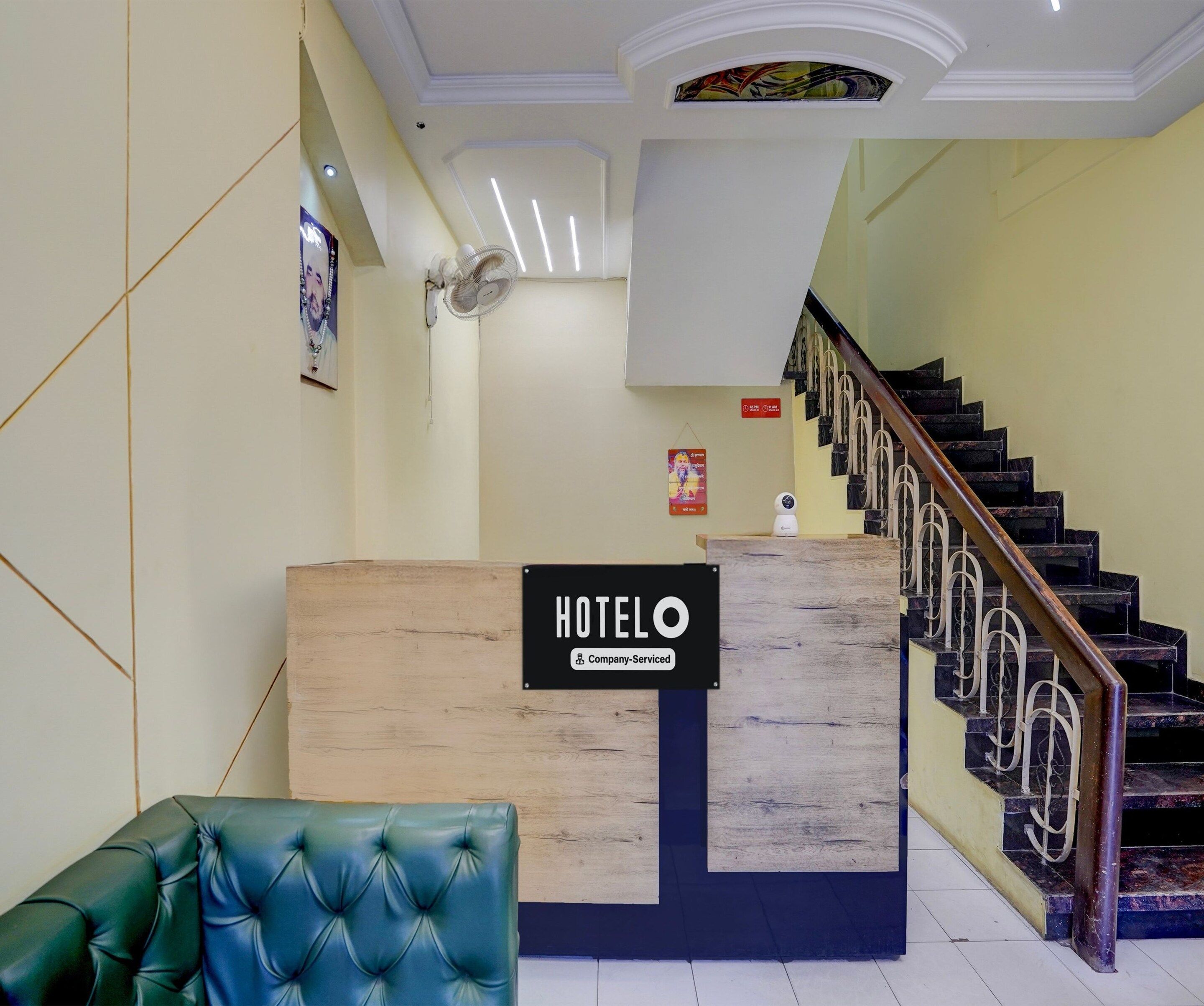 Un mostrador de recepción de hotel con un cartel que indica servicio de empresa. Se ve una escalera de fondo, con barandilla de madera y balaustradas de metal.