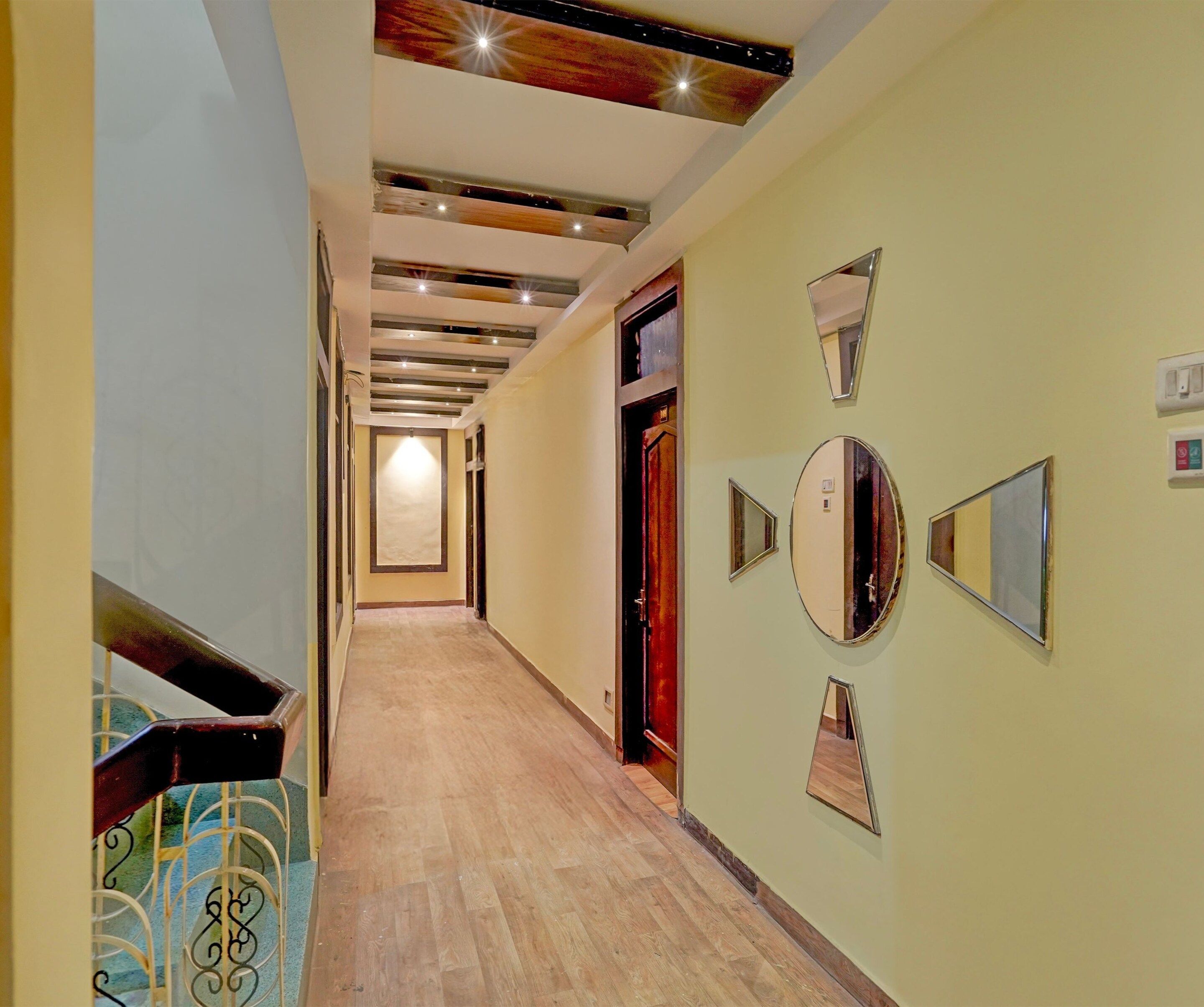 A hallway with a wooden floor, a staircase with metal railings, and a door with a mirror.
