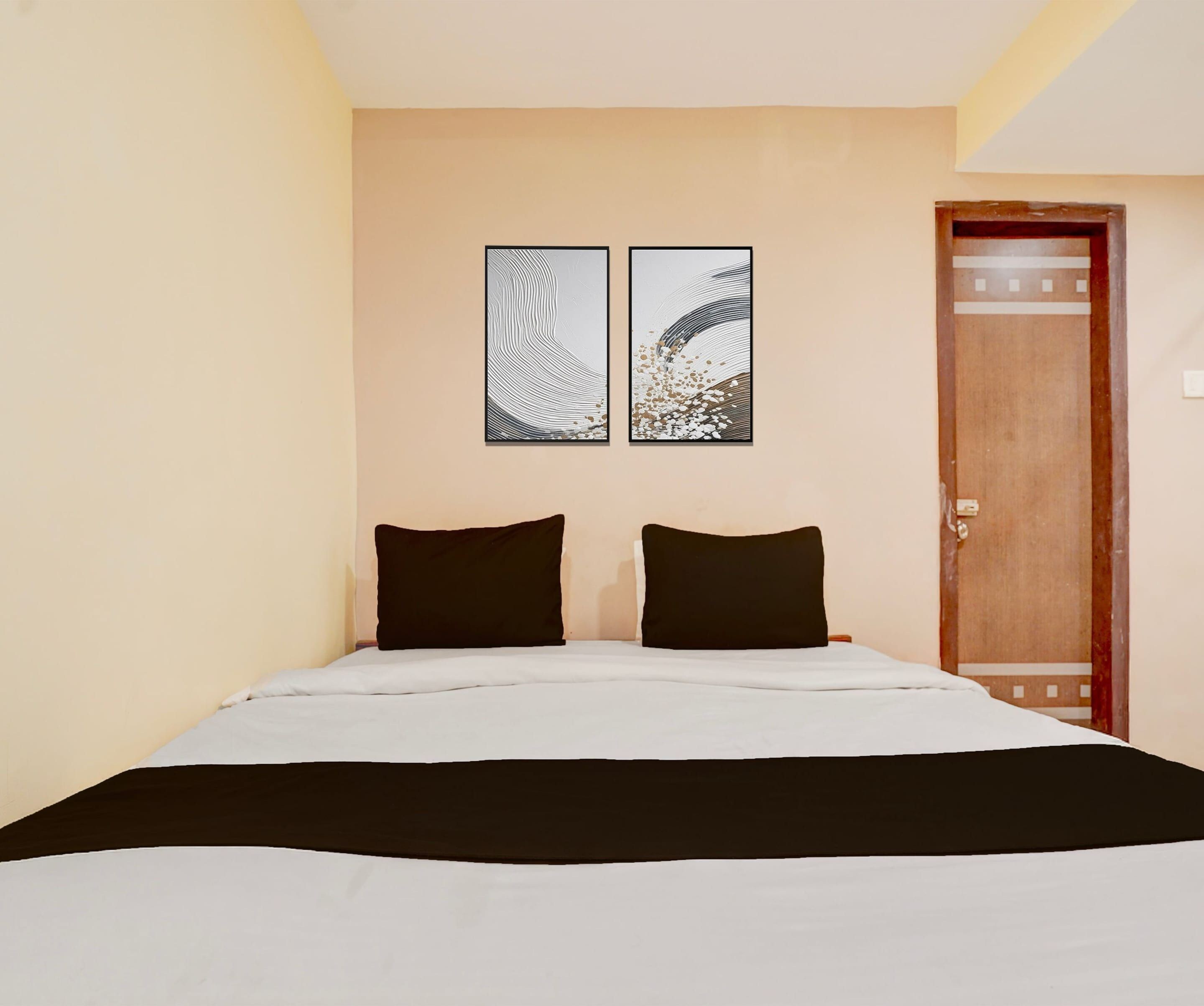 A hotel room with a bed, two black pillows, and two wall-mounted artworks.