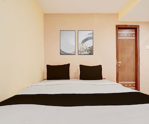 Habitación de hotel con una cama, dos almohadas negras y dos obras de arte colgadas en la pared.