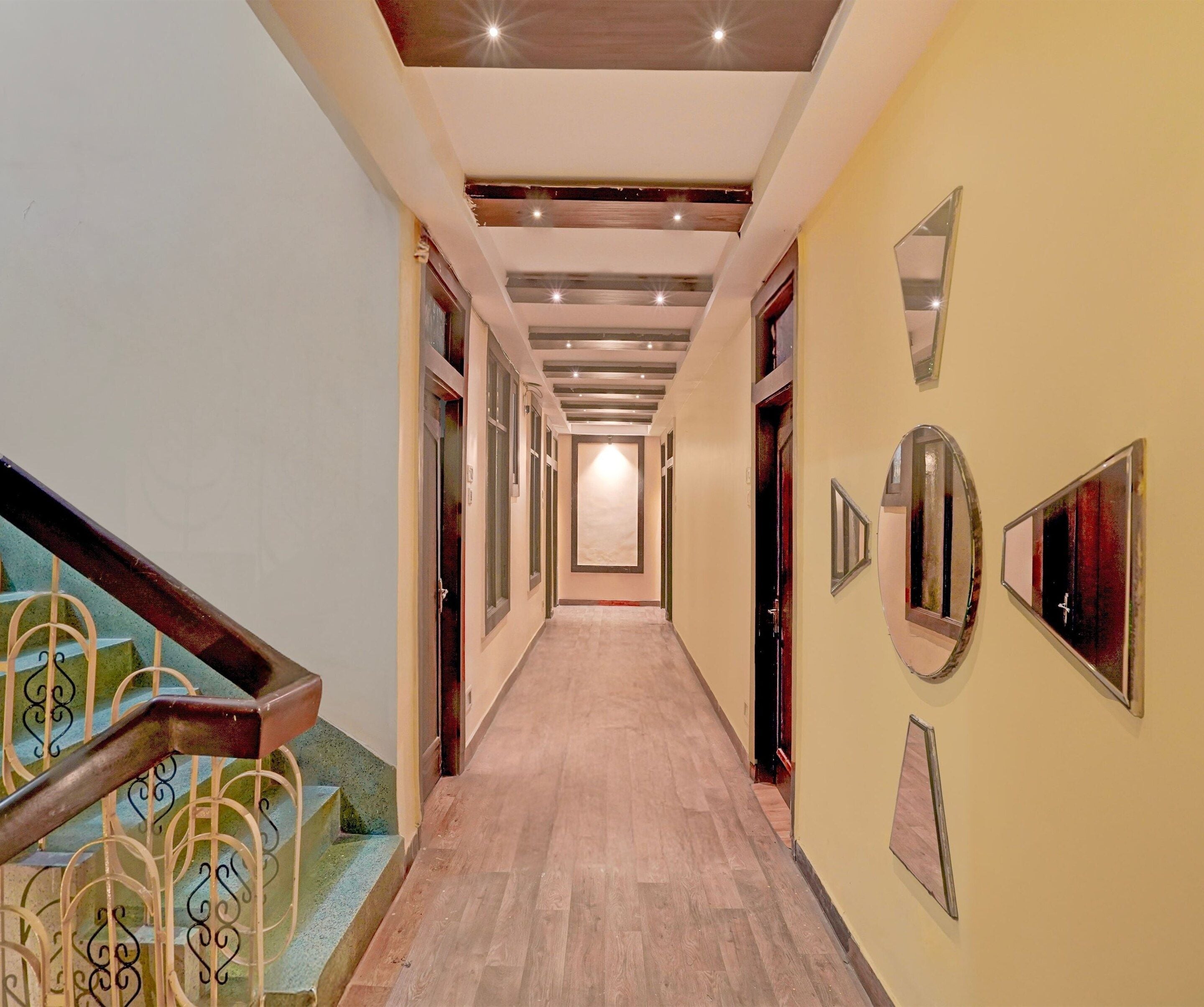 A hallway with a wooden floor, a staircase with ornate metal railings, and walls adorned with mirrors and framed pictures.