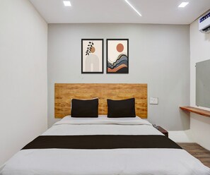 Una camera d'albergo con un letto, una testiera in legno, due cuscini neri e due opere d'arte incorniciate appese al muro.