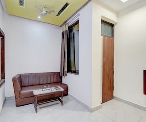 Una habitación con un sofá de cuero marrón, una pequeña mesa de madera, un ventilador de techo, una ventana con cortinas y una puerta de madera.