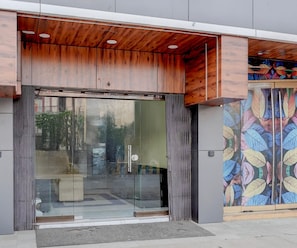 Una entrada moderna a un edificio con puerta de cristal, techo de madera y una pared con un estampado de hojas de colores.