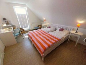 A bedroom with a bed, two bedside tables, a desk, a chair, and a window. - Eric's Holiday Home (Krummhoern)