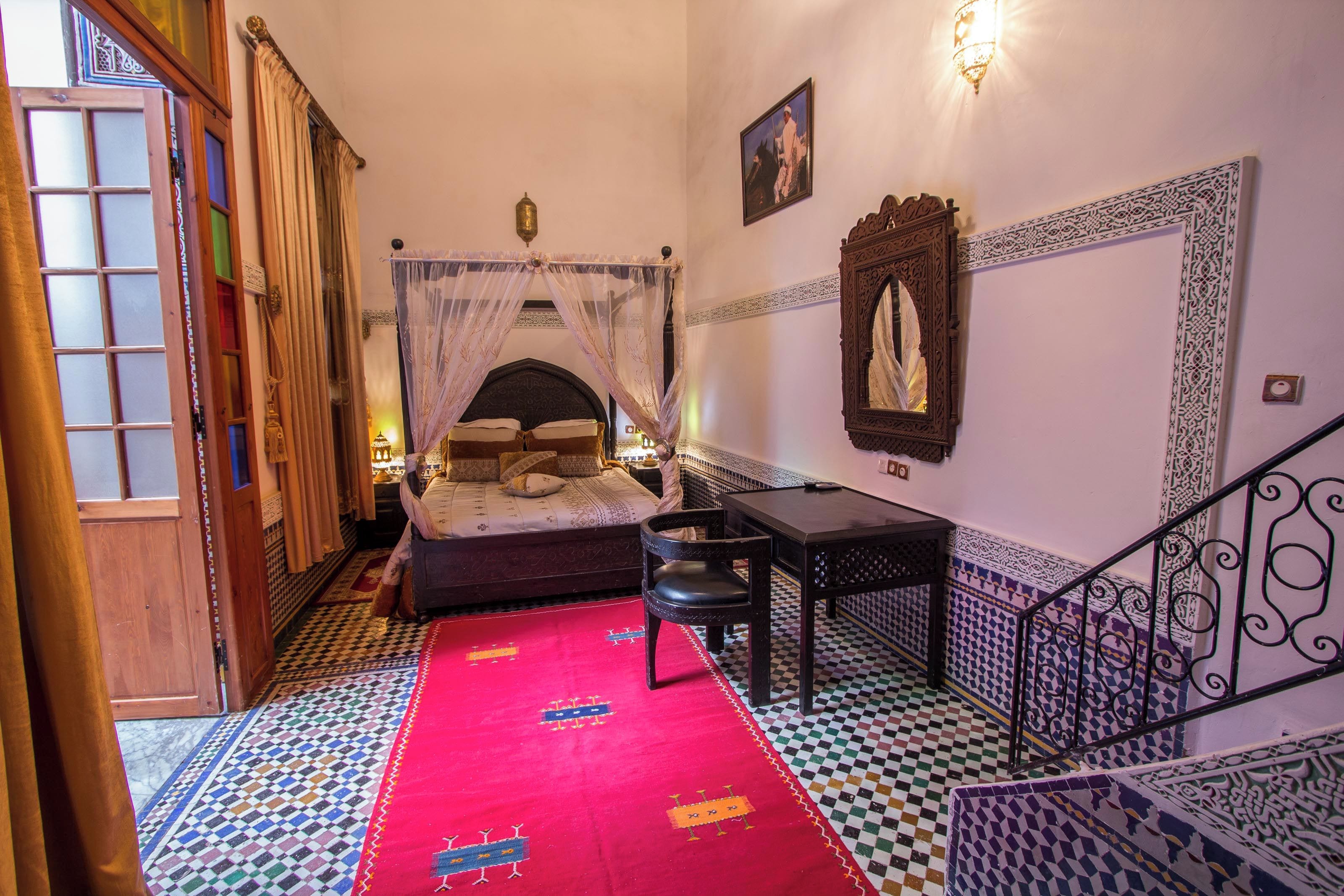 Une pièce comprenant un lit, une table, une chaise, une moquette rouge et un escalier.