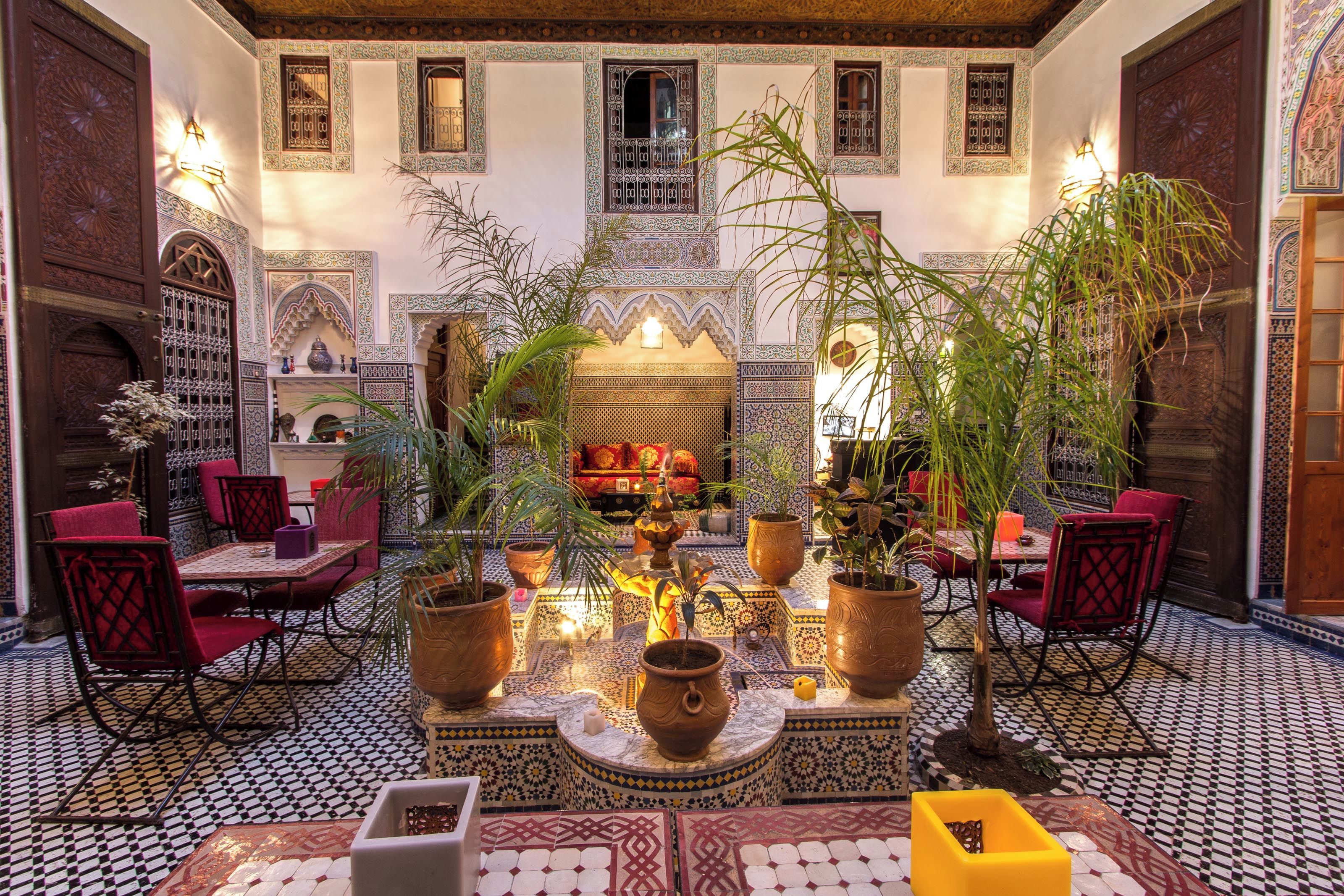Un interior tradicional marroquí con una fuente central, zona de estar y paredes ornamentadas.