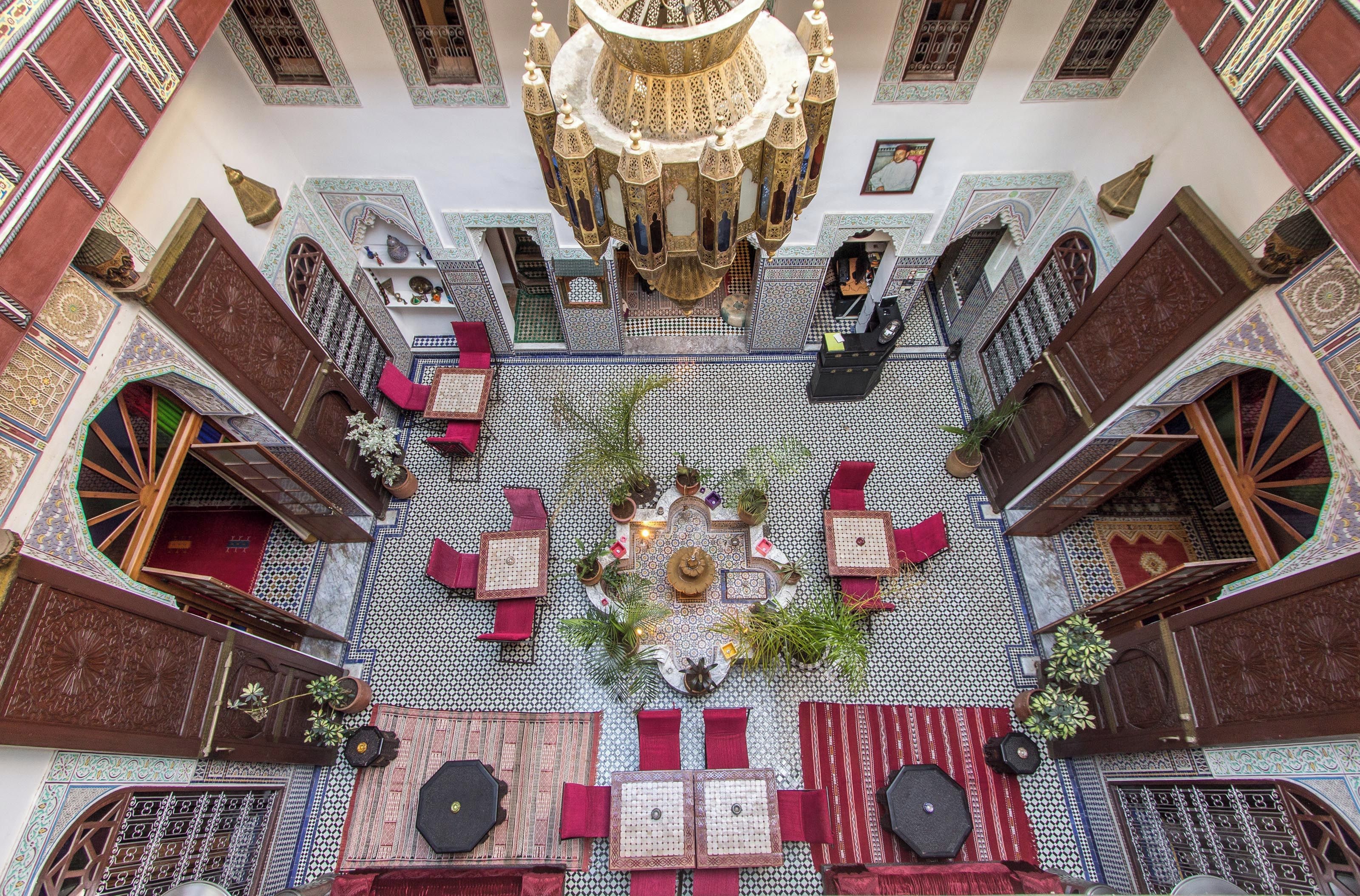 A traditional Moroccan interior with a central courtyard, ornate ceiling, and patterned floor tiles.