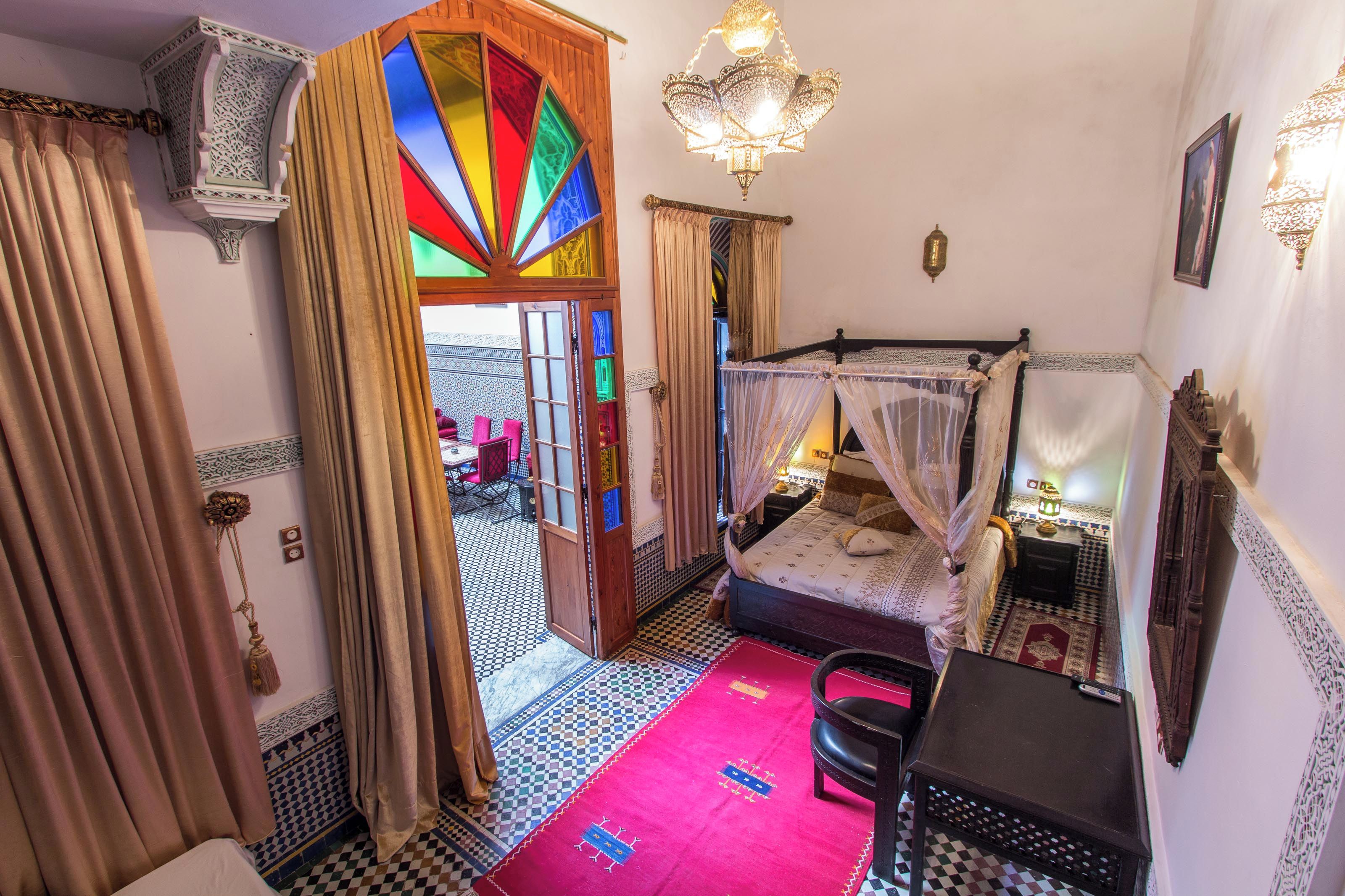 Una habitación con cama, escritorio, silla y una puerta con vidrieras de colores.