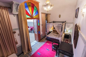 A room with a bed, a desk, a chair, and a colorful stained glass door. - Ryad Naila  (Fès)
