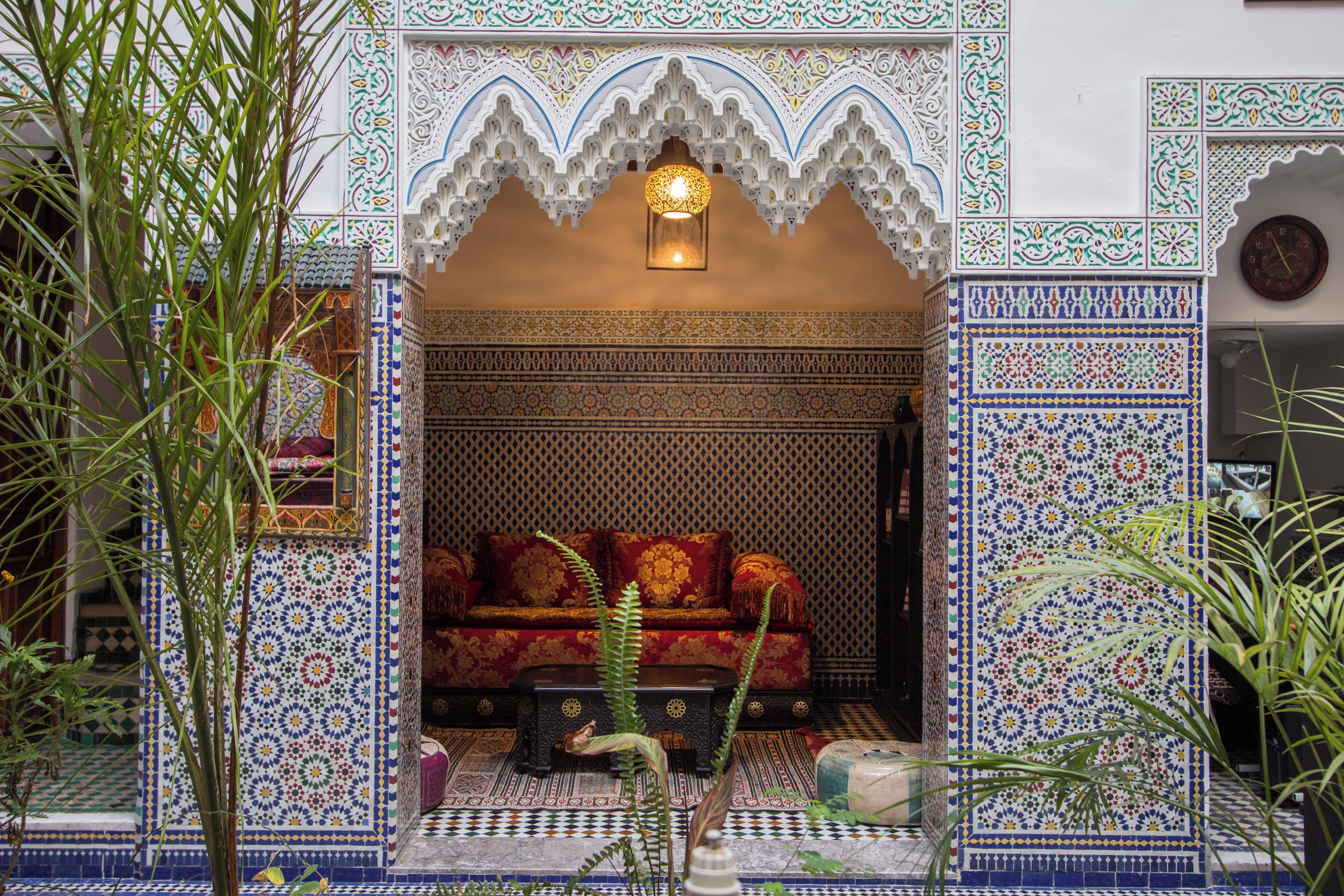 Una entrada ornamentada con detalles en mosaicos, un área de descanso con cojines estampados y una lámpara colgante.